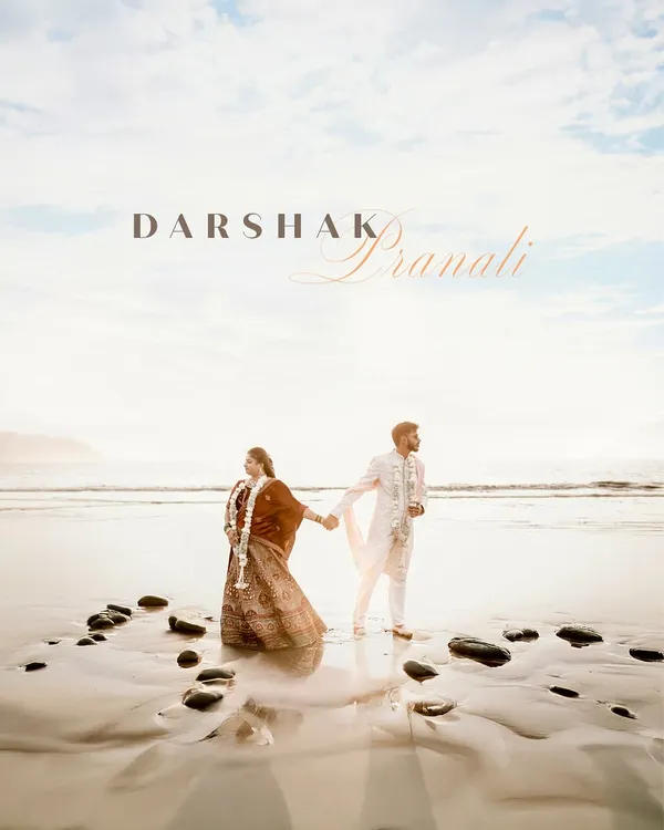 A breathtaking destination wedding portrait on the beach. The couple holds hands against a vast ocean and a beautiful sky, creating a truly epic and romantic memory of their special day.