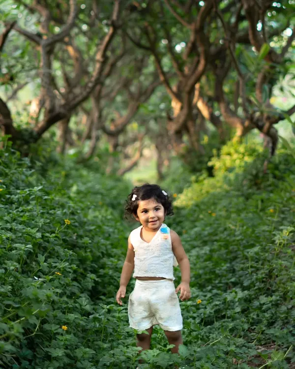 A beautiful portrait of a toddler standing in a field of lush green clover. The winding path of trees creates a magical, forest-like setting.