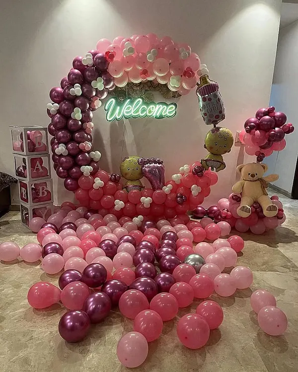 A beautiful crescent moon balloon structure for a baby girl's welcome. The setup includes a "Welcome" neon sign, teddy bears, and a sea of pink and magenta balloons on the floor for a dreamy effect.