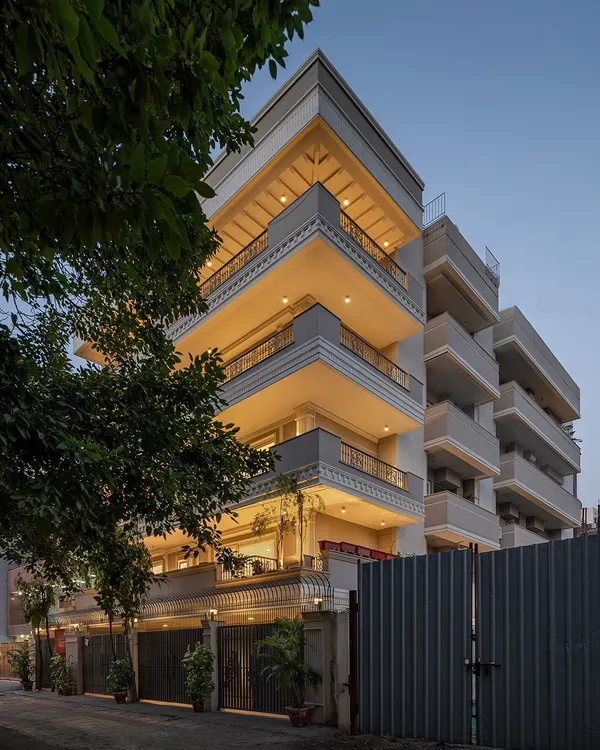 The KAIRA residence viewed from the street at dusk. The facade's neo-classical details, including layered cornices and decorative railings, are highlighted by integrated lighting, creating a warm and inviting presence.