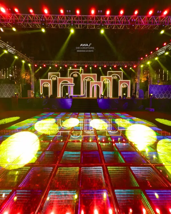 A high-energy Sangeet stage with a multi-level, LED-lit backdrop and a reflective dance floor, ready for a night of performances.