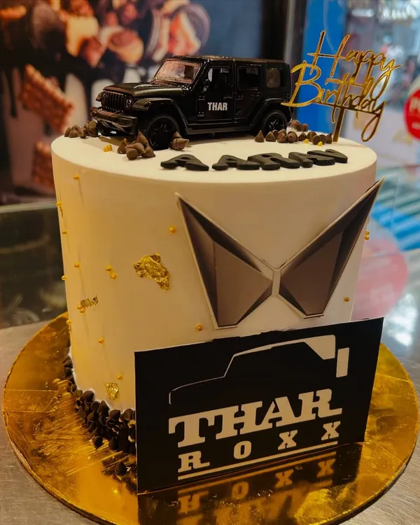 A sleek and stylish cake for a Mahindra Thar enthusiast. This design features the new Mahindra logo, a "Thar Roxx" plaque, and a detailed model of the black SUV on top.