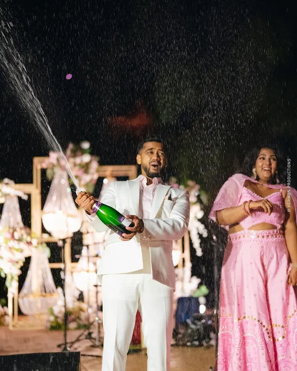 A moment of pure celebration! The groom pops a bottle of champagne at their glamorous outdoor cocktail party.