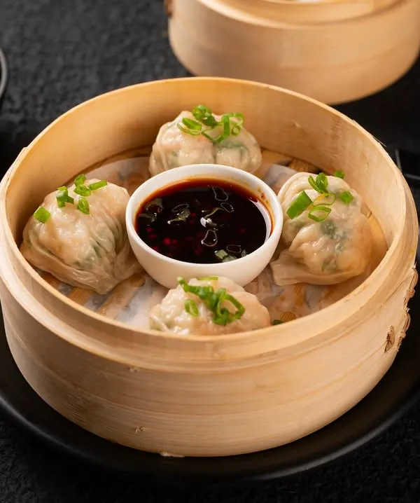 A classic shot of steamed dim sum in a bamboo basket, perfectly styled for an online delivery menu. The image is clean, bright, and clearly shows the customer what they will receive.