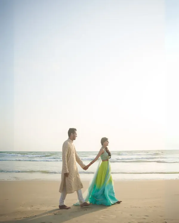 A beautiful, wide-angle shot of a couple walking hand-in-hand on a serene beach, showcasing their connection against the vastness of the ocean.