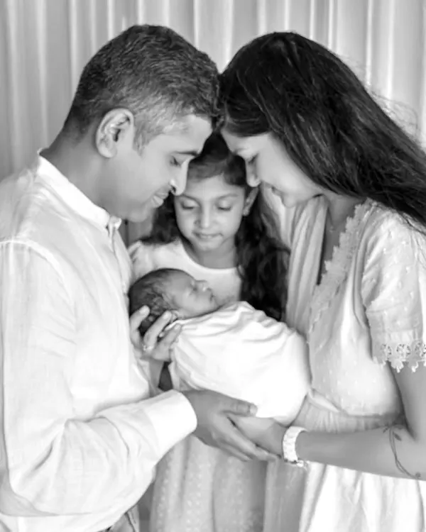A classic black and white family portrait showing parents and an older sister lovingly gazing at their newborn baby, capturing a moment of pure love and connection.