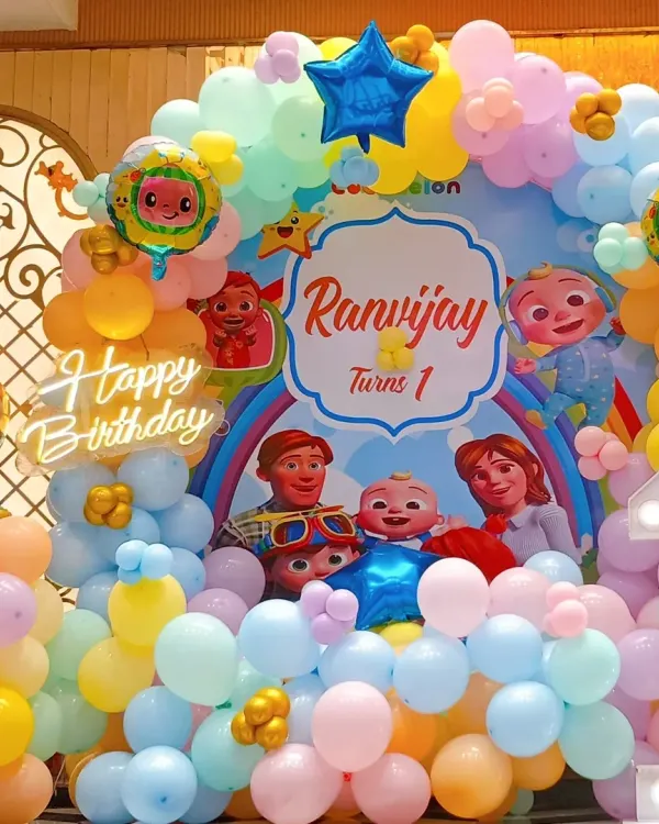 A close-up of a vibrant Cocomelon birthday setup for a first birthday. We included a custom backdrop with all the main characters, themed foil balloons, and a colorful balloon arch.