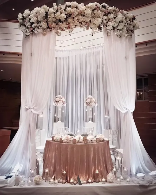 This grand, all-white decor is perfect for an elegant reception or ring ceremony. The flowing drapes and dramatic floral arch create a breathtaking canopy over the main table, exuding pure sophistication.