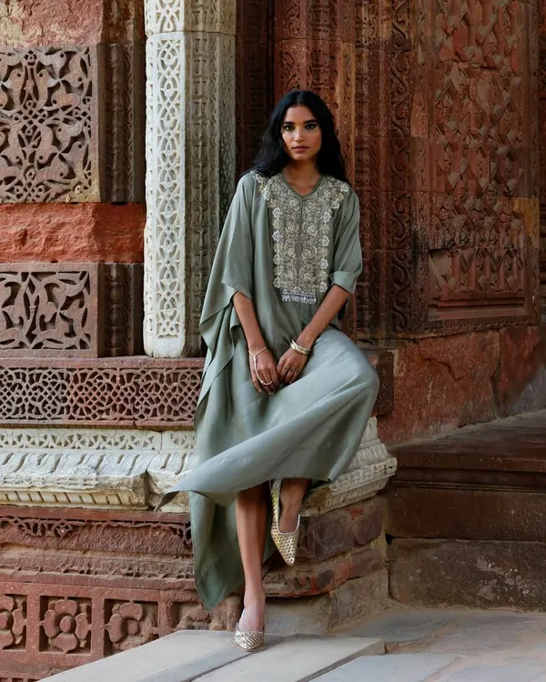 The beauty of a timeless silhouette against a historic backdrop. This model wears a sage green kaftan with an embroidered yoke, a perfect blend of comfort and elegance.