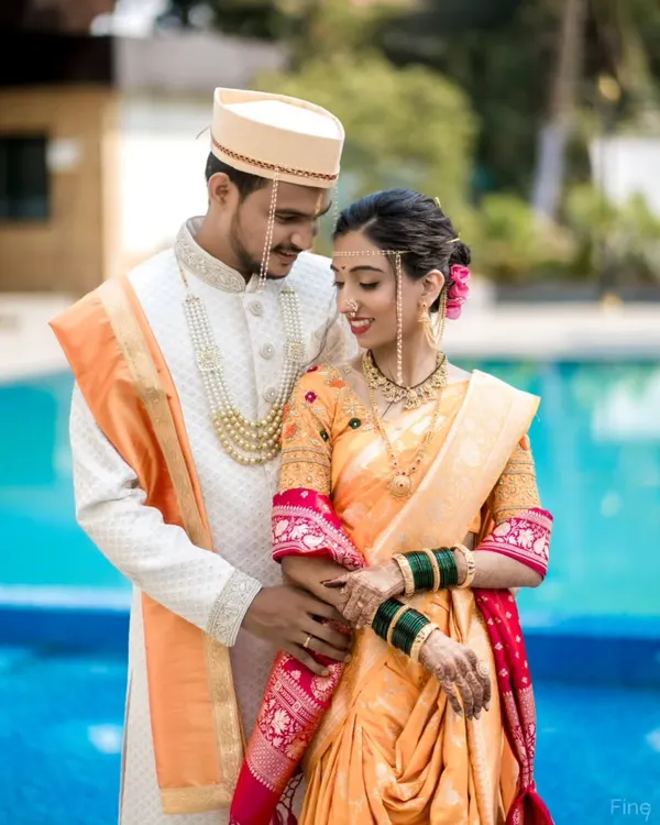 A classic Maharashtrian wedding portrait. The couple's coordinated attire, from the groom's Pheta to the bride's Nauvari saree, is captured beautifully against a simple, elegant backdrop.