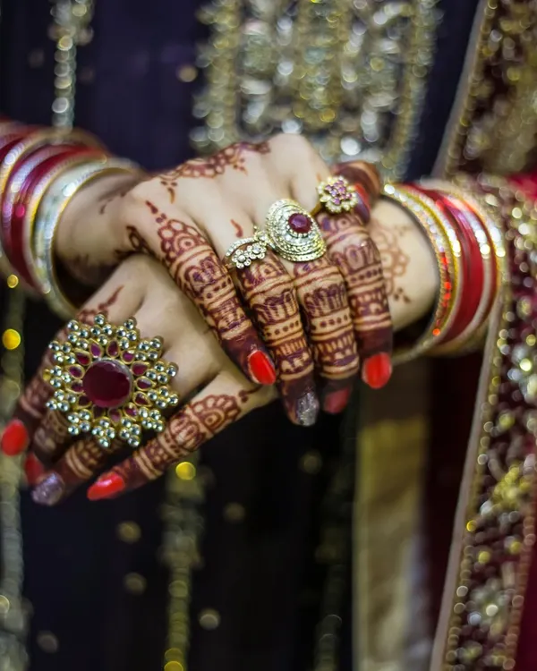 A close-up shot focusing on the bride's hands, showcasing the beautiful bridal rings, bangles, and intricate mehendi design.