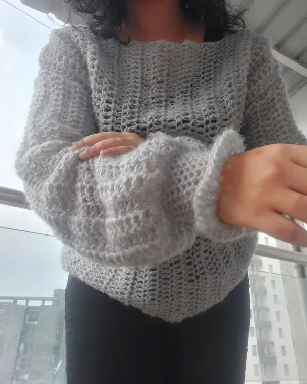 This is the Vevitha Sweater, crafted from a soft and fuzzy mohair yarn. The open mesh stitch creates a light and airy feel, while the balloon sleeves add a touch of drama.