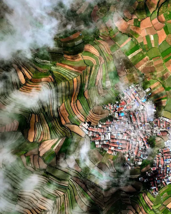 A top-down drone photograph of Poombarai Village in Kodaikanal, Tamil Nadu. The terraced fields and the village nestled among them create a stunning, almost abstract pattern when viewed from above.