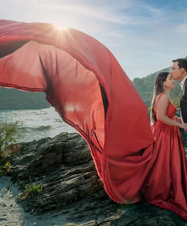 With the sun setting over the river, her red gown catches the wind, creating a moment of pure cinematic magic. This is the kind of epic, dramatic pre-wedding shot that becomes the poster for your love story.