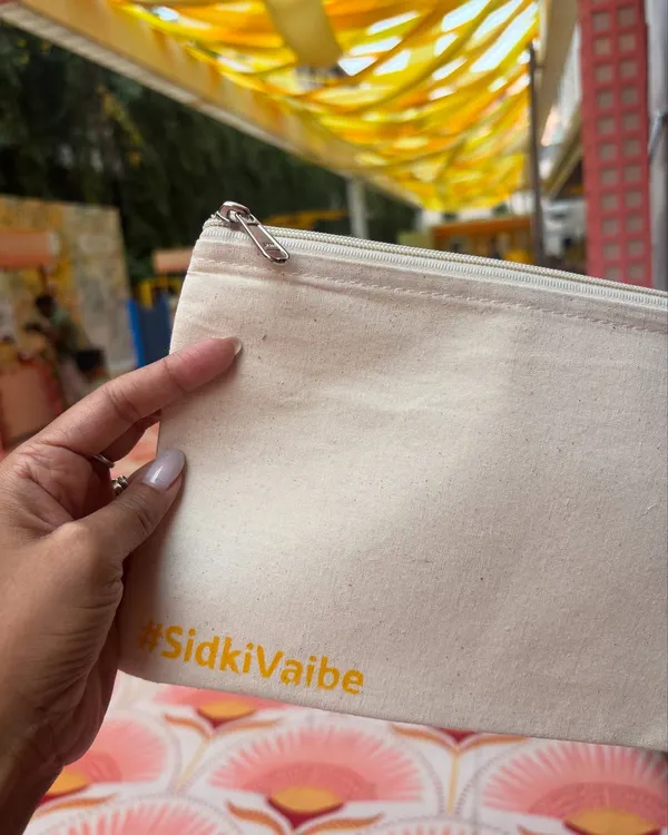 A close-up of a blank pouch being personalized with the custom #SidkiVaibe hashtag for a Haldi party. This first stamp is the beginning of a unique creation that guests will treasure as a memory of the special day.