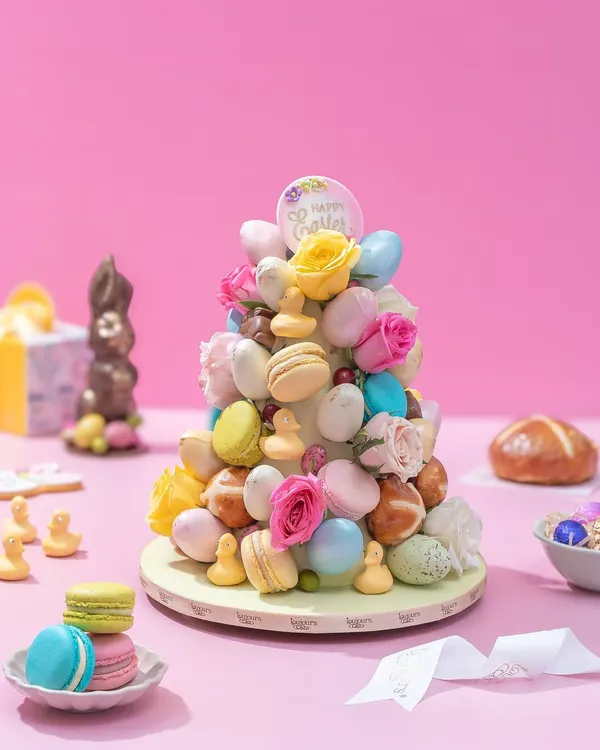 My spectacular Easter Treat Tower, a cone adorned with colorful macarons, mini hot cross buns, fresh roses, and chocolate eggs. It's a stunning centerpiece for any Easter celebration.