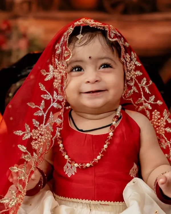 The radiant smile of a little girl dressed in a beautiful red and white traditional outfit. The delicate veil and jewelry complete this stunning portrait.