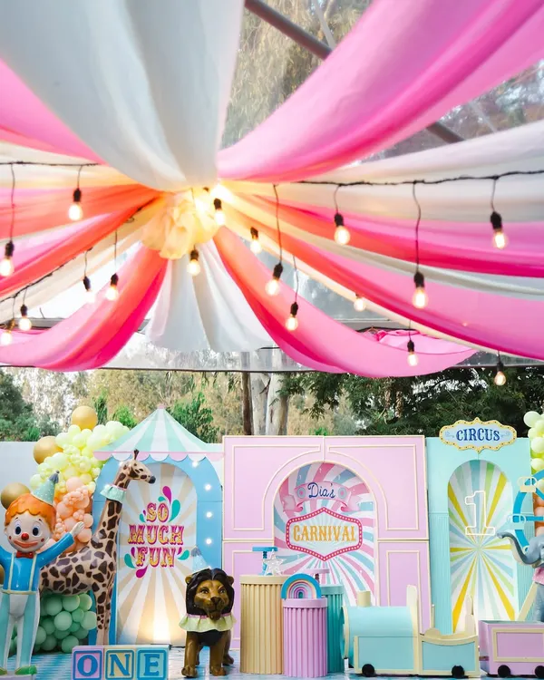 A breathtaking view of Dia's carnival, with colorful draped fabrics and string lights creating a magical big-top tent effect. The backdrop is filled with custom-built circus props and playful characters.
