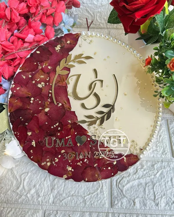This is a 10-inch round resin frame where I preserved red rose petals from a varmala in a crescent moon shape. A custom couple logo, names, and the wedding date are featured in gold.
