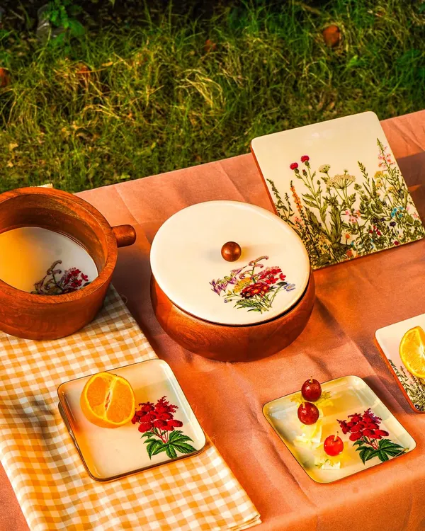A beautiful outdoor picnic scene featuring hand-painted wooden tableware. The 'golden hour' lighting creates a warm, inviting atmosphere that's perfect for lifestyle brands.