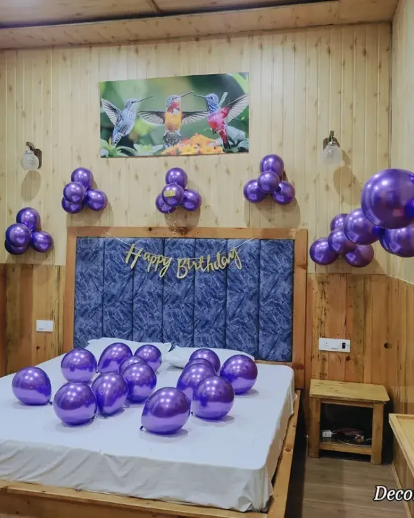 Sometimes, simplicity is key. This basic room decor features clusters of metallic purple balloons on the wall and scattered on the bed, with a simple 'Happy Birthday' banner. It's an easy and affordable way to create a surprise.