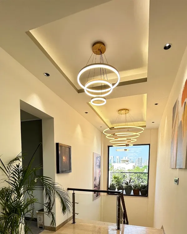 This stunning double-height hallway features a series of modern ring chandeliers and a tray ceiling design, creating a dramatic and luxurious sense of arrival.