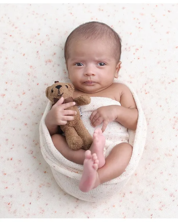 A classic potato sack pose with a twist. This awake and expressive newborn holds a tiny teddy bear, making for an incredibly endearing and memorable portrait.