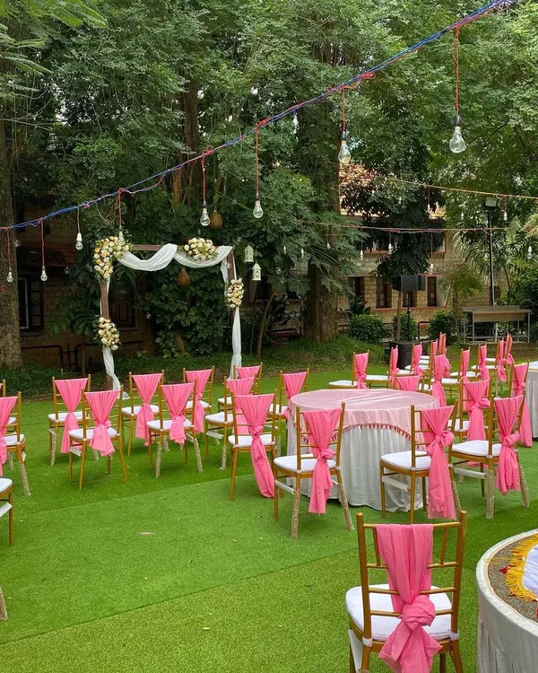 A beautiful daytime wedding reception setup at UTC. The vibrant pink sashes on the chairs add a pop of color to the lush green lawn, while the wooden arch creates a perfect focal point for the ceremony.