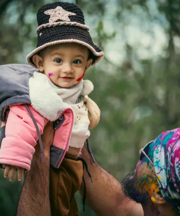 A father joyfully lifts his son into the air during his very first Holi celebration. The baby's smile and the colorful background perfectly capture the happiness of this family festival.