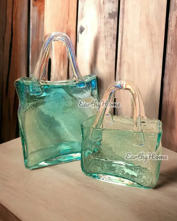 This hand-blown glass handbag vase is one of our most talked-about items. Its unique shape and beautiful aqua color make it a stunning centerpiece or a standalone piece of art, available in two sizes.
