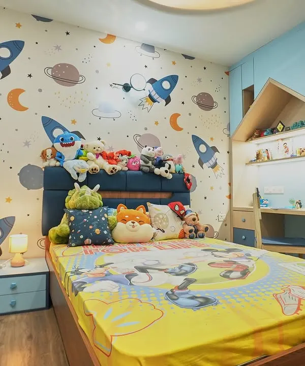 This space-themed bedroom is ready for adventure. The wallpaper is filled with rockets and planets, and the bed is piled high with cuddly friends. The house-shaped study nook is a cozy spot for reading and drawing.