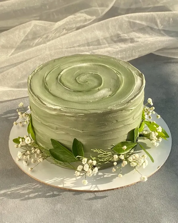 I love the simple beauty of this sage green cake. The rustic, textured frosting is complemented by a delicate wreath of baby's breath and leaves, creating a natural and modern look.