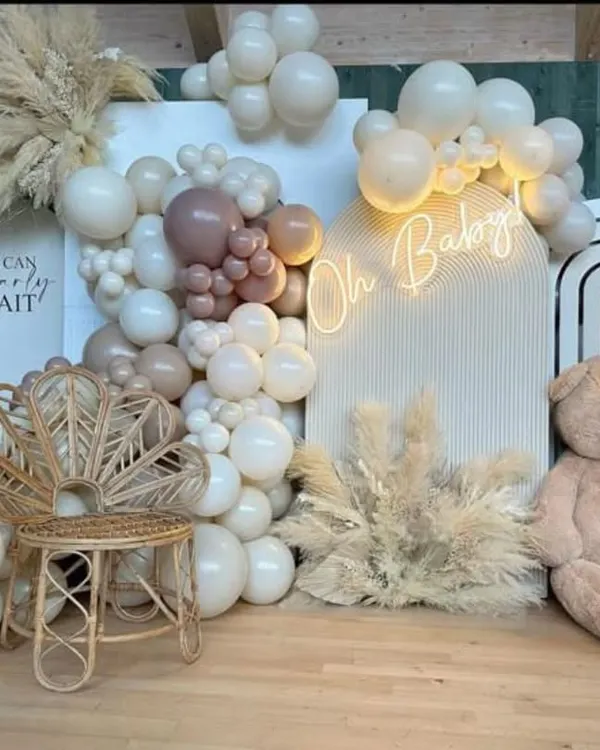 A beautiful boho-chic baby shower setup, perfect for a modern and stylish celebration. This design features a neutral color palette with pampas grass, a custom "We Can Bearly Wait" sign, a comfortable peacock chair for the mom-to-be, and a full organic balloon garland, creating a warm and inviting atmosphere.