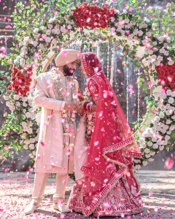 A magical moment frozen in time as the couple is showered with rose petals after their varmala ceremony. This shot captures the pure, unscripted joy and the grand scale of a beautiful celebration, framed by a stunning floral arch.