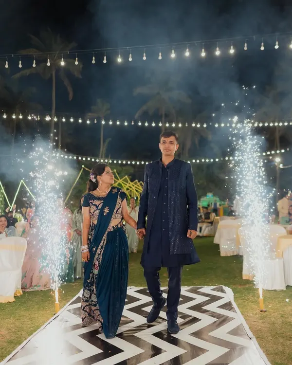 A picture-perfect Sangeet entrance. The couple makes their way down a stylish black-and-white chevron-patterned aisle, flanked by celebratory cold pyro sparklers and set under a canopy of warm string lights.