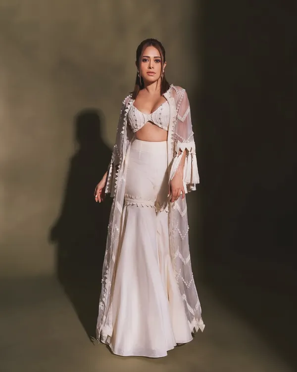 Pearls and tassels make this white indo-western outfit on Nushrratt Bharuccha a true statement piece. The flared pants and detailed cape are perfect for a modern, festive look.