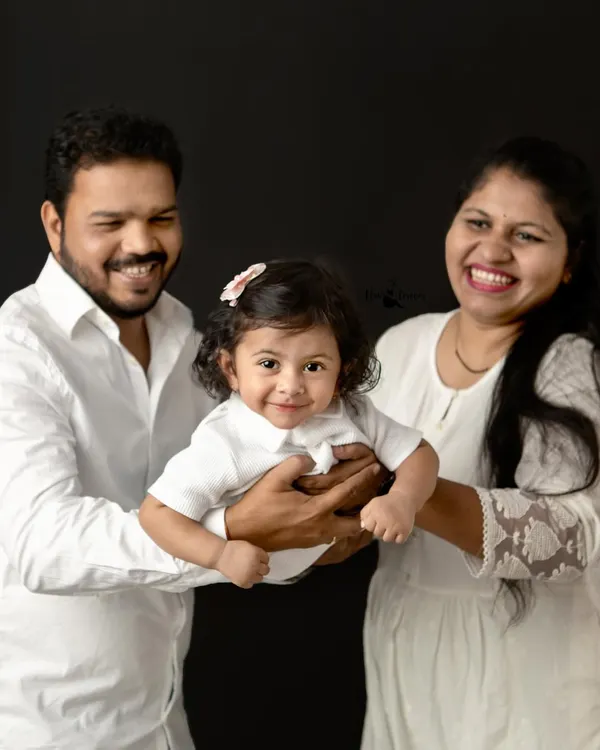 A perfect family portrait, full of laughter and joy. Holding their little one together, this family's happiness is radiant against the classic black studio background.