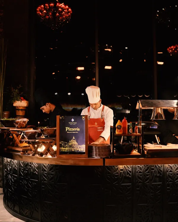 The heart of our Italian corner. A chef at the Pizzeria station, meticulously preparing fresh pizzas for guests in a beautifully designed, ambient setting.
