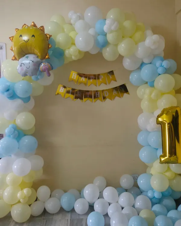 A cheerful sun-themed first birthday decoration. This simple balloon arch in pastel yellow and blue is perfect for a small home celebration.