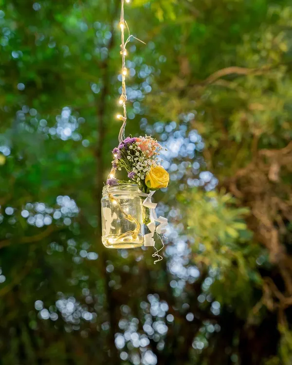 A simple mason jar filled with a small bouquet and fairy lights, hanging from a tree. This is a perfect example of how I use small, creative details to add a touch of rustic charm to an outdoor event.
