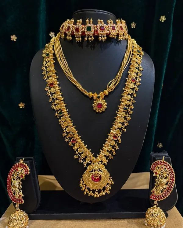 This is a classic temple jewellery set for rent, featuring a choker, a long necklace (haram), and matching jhumka earrings with red and green stones.