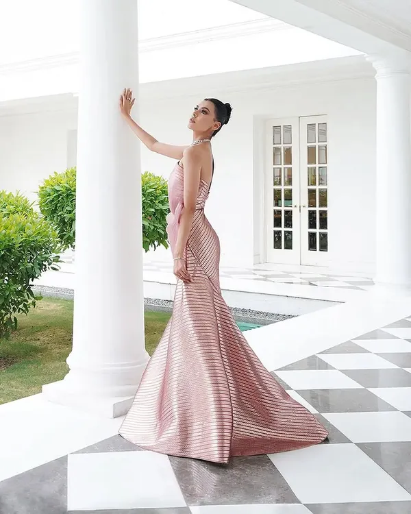 A full-length shot of a stunning metallic pink gown by Amit Aggarwal. The structured, pleated fabric creates a futuristic mermaid silhouette, styled to look statuesque and elegant against the classic architecture.