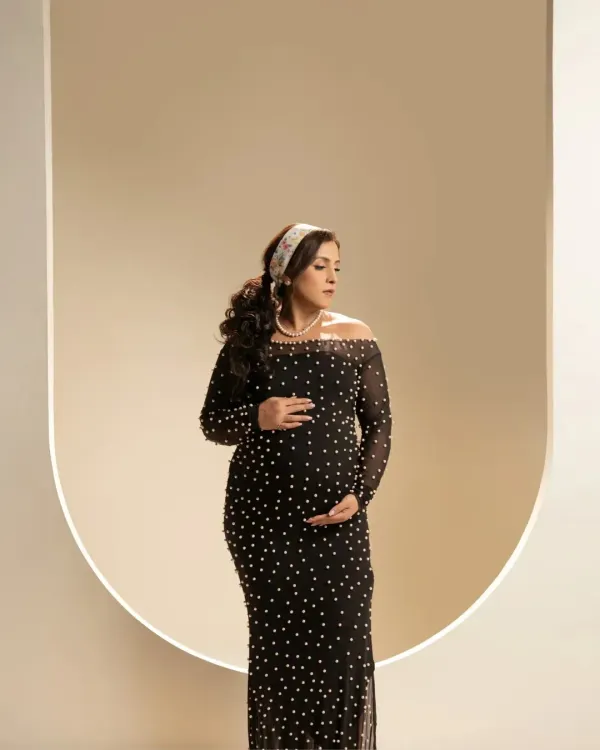 A portrait of pure elegance. The mother-to-be is captured in a stunning black pearl-studded gown against a modern, arched backdrop, creating a look that is both contemporary and timeless.