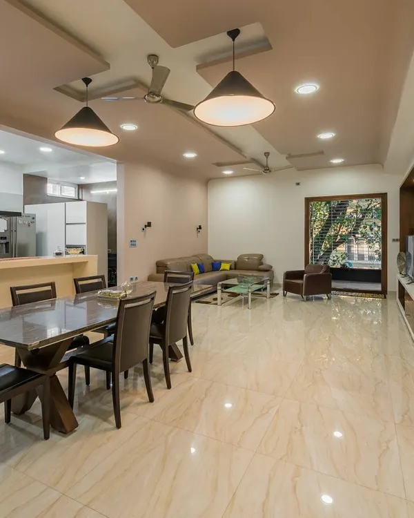 An open-concept living and dining area in a large Bangalore residence. The polished marble floors and neutral color palette create a bright, expansive feel, while the layout ensures a practical flow between the kitchen, dining, and lounge zones.
