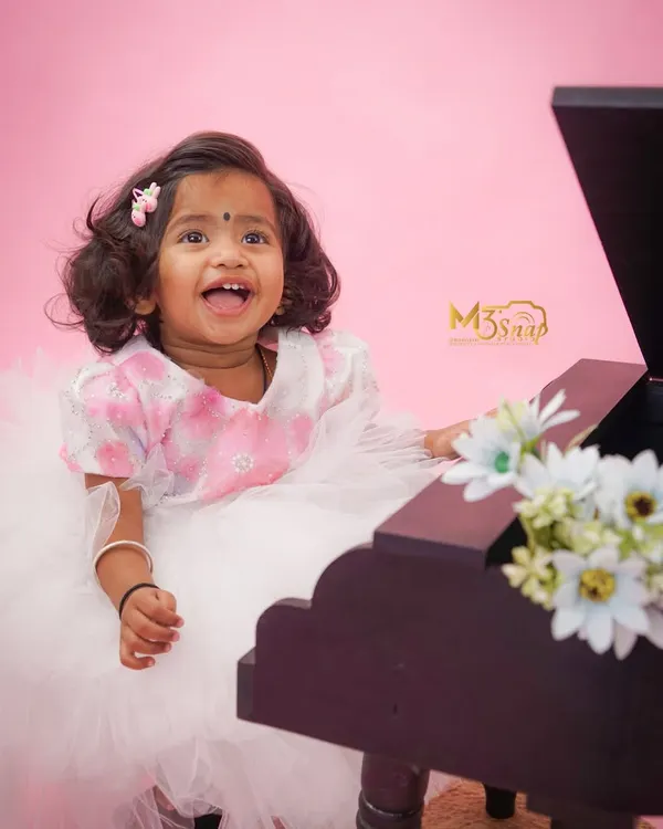 What a happy smile. This little girl is having a great time at her milestone session, playing with a miniature piano against a lovely pink backdrop.