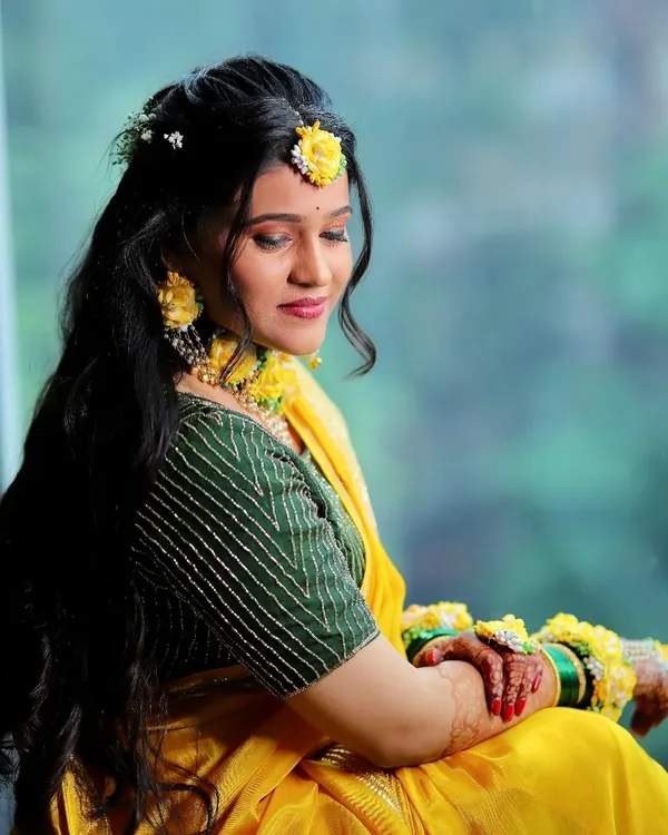 A classic Haldi look. The bride is glowing, with minimal makeup that enhances her natural beauty, perfectly matching her yellow saree and floral jewelry.