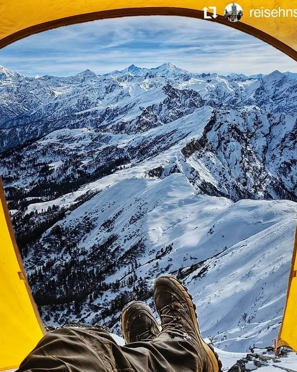 The ultimate room with a view. This is the perspective from inside a tent pitched high in the Himalayas, offering an unparalleled, panoramic vista of a vast, snow-covered mountain range.