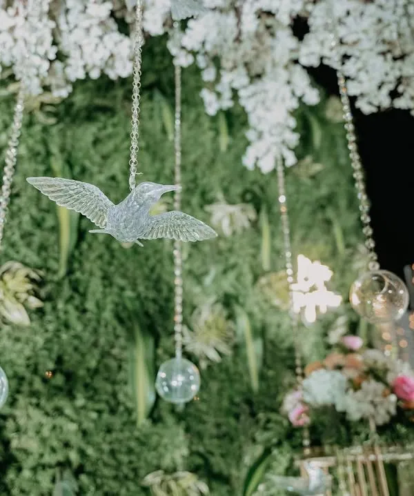 A close-up of a lush green foliage wall with a neon 'Better Together' sign and delicate hanging crystal birds. It's these small, thoughtful details that create a magical atmosphere.