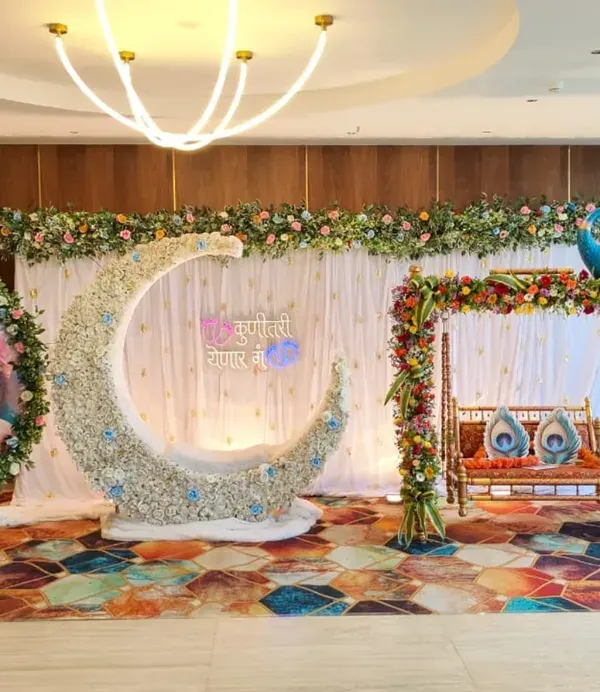 A grand and traditional Dohale Jevan setup we created, featuring a beautiful peacock-themed jhula for the mother-to-be. The stage includes a custom printed backdrop of Yashoda and Krishna, a floral moon-shaped seat, and a vibrant, colorful carpet.