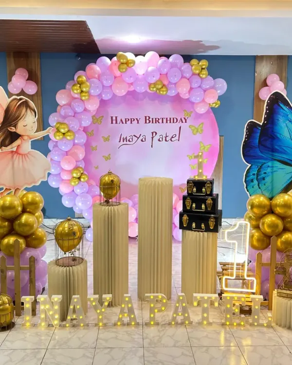 A magical fairy and butterfly theme for a first birthday. This setup uses pastel purple and pink balloons, golden chrome accents, life-sized fairy cutouts, and illuminated marquee letters to create an enchanting garden scene.